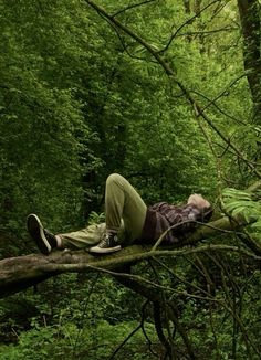 a man laying on top of a fallen tree in the forest with his head down