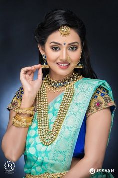 a woman in a green and blue sari with gold jewelry on her neck, posing for