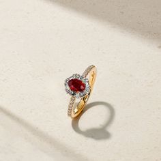 A glowing red ruby lays at the center of this meticulously crafted ring that's framed by a halo of twinkling round and baguette diamonds. Additional petite round diamonds sparkle along each end of the comfort fit shank to complete the look. Make this elegant and timeless adornment apart of your everyday jewelry rotation. Metal: 18kt Gold Ruby Weight: 0.60 ct. Round Diamond Weight: 0.25 ct. Baguette Diamond Weight: 0.22 ct. Measurements: 10.0 mm length *Please note that the listed ct. weights are Luxury Red Ruby Ring Baguette Cut, Luxury Red Baguette Cut Ruby Ring, Luxury Ruby Ring With Diamond Halo, Luxury Ruby Diamond Ring With Halo, Luxury Ruby Halo Diamond Ring, Luxury Ruby Halo Setting Wedding Ring, Luxury Ruby Wedding Ring With Halo Setting, Luxury Ruby Halo Wedding Ring, Red Diamond Ring With Baguette Cut