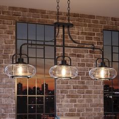 three lights hanging from the ceiling in front of a brick wall and window with cityscape