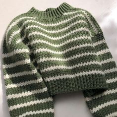 a green and white knitted sweater laying on top of a table