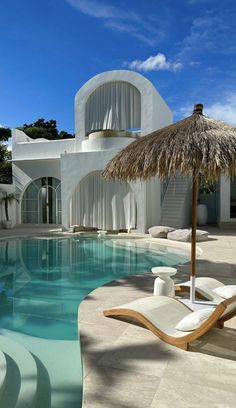 an outdoor swimming pool with chaise lounge chairs and thatched umbrella in the foreground