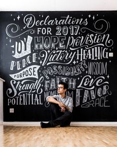 a man sitting on the floor in front of a chalkboard with words written all over it