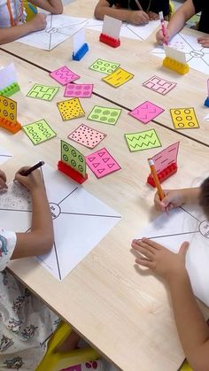 several children sitting at a table with paper and pencils on it, making shapes