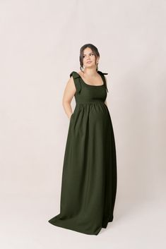 a woman in a long green dress standing with her hands on her hips and looking off to the side