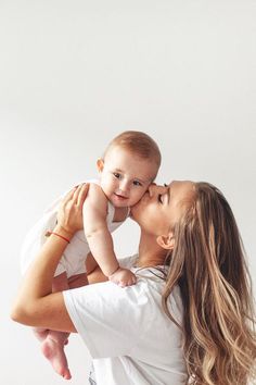 a woman holding a baby in her arms and kissing it's face with the other hand