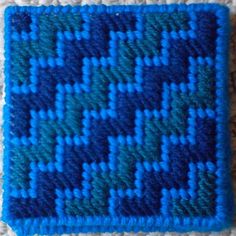 a close up of a blue and green knitted square on a white carpeted surface