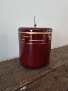 a red and gold container sitting on top of a wooden table next to a white wall