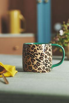 a leopard print coffee cup sitting on top of a table next to a yellow towel