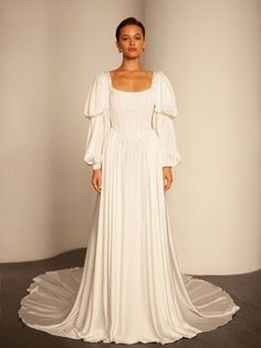 a woman in a white wedding dress standing on a gray floor with her arms behind her back