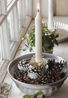 a white candle is sitting in a bowl filled with pine cones