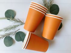 three orange cups sitting next to each other on top of a white table with green leaves