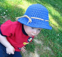 a young boy wearing a blue crocheted hat on top of his head while sitting in the grass