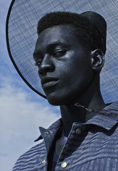 a young man with black paint on his face wearing a mesh headdress against a blue sky