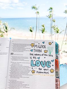 an open book sitting on top of a table next to the ocean and palm trees