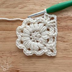 the crochet square is being worked on by a green handled knitting needle,