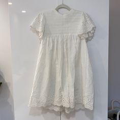 The Stunning Nancy Dress By Steele Features A Feminine, Relaxed Fit With Shirred Panel And Short Ruffle Sleeves With Broderie Detailing At Edge. Nancy Also Features A High Neckline With Neck Band, Button Closure At Back Neckline And Delicate Broderie Scallop Detail At Hem. This Style Is Fully Lined And Sits Above The Knee. Fabric: Cotton Broderie White Dress With Cutwork Hem For Brunch, Eyelet Short Sleeve Dresses For Brunch, Short Sleeve Eyelet Dress For Brunch, Chic Dresses With Cutwork Hem And Short Sleeves, Short Sleeve Midi Dress With Broderie Anglaise For Brunch, Broderie Anglaise Midi Dress With Short Sleeves For Brunch, Broderie Anglaise Mini Dress With Short Sleeves For Brunch, Summer Eyelet Dress With Short Sleeves, Elegant Eyelet Beach Dress