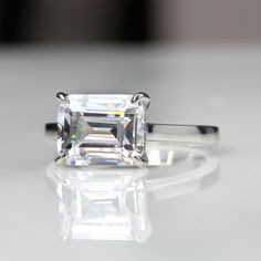 an emerald cut diamond ring on a white surface