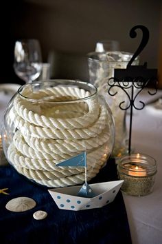 a table topped with a bowl filled with white rope next to candles and seashells