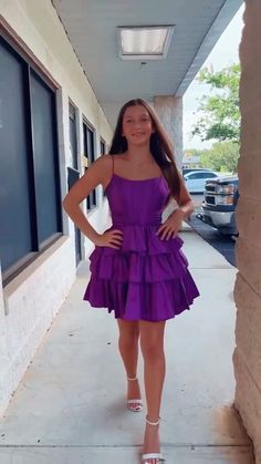 a woman in a purple dress is standing on the sidewalk