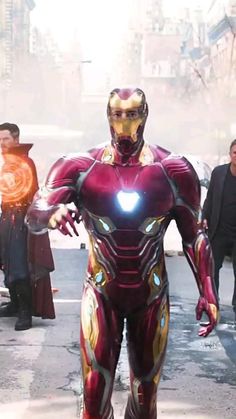 iron man standing in the middle of a street with other people around him and looking on