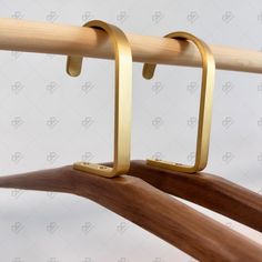 a pair of wooden clothes hangers with brass colored metal bars hanging from the top