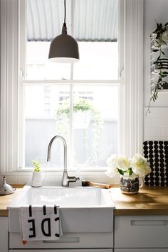 a kitchen sink sitting under a window next to a wooden counter top with white flowers