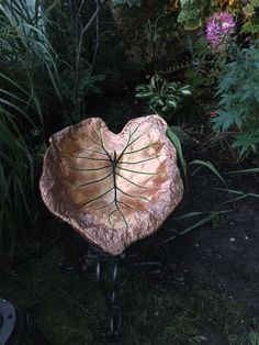 a heart shaped planter sitting on top of a metal stand in front of some plants