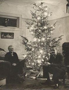 an old black and white photo of two people sitting in front of a christmas tree