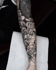 a person's arm with flowers on it and a black cat in the background