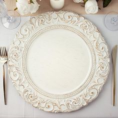 an empty plate on a table with silverware and white flowers in the vases