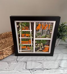 a shadow box with scissors and plants in it on a table next to a wicker basket