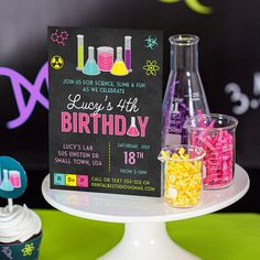 a science themed birthday party with cupcakes and drinks on a cake stand in front of a chalkboard sign