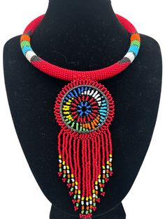 Add a touch of African beauty to your outfit with this beaded necklace. Handcrafted using high-quality beads and brass metal, this necklace is a perfect addition to any jewellery collection. The pendant's unique tassel design adds a touch of elegance to its ethnic and regional style. Its red colour symbolizes passion and love, making it a great gift to show appreciation to a loved one. This necklace is perfect for any occasion, from a casual day out to a formal event. With its intricate beaded design, it is sure to catch the eye of anyone who sees it. Whether you wear it to work or a night out, this necklace will add a touch of glamour to your outfit.  Neck Width - 18 inches. Colour: Red Material: Beads, Brass Festival Beaded Necklaces With Tassels And Round Beads, Traditional Red Beaded Necklaces With Dangling Beads, Traditional Red Beaded Necklace With Dangling Beads, Traditional Beaded Fringe Necklace As Gift, Artisan Red Beaded Necklace With Dangling Beads, Artisan Red Beaded Necklace With Round Beads, Traditional Adjustable Beaded Fringe Necklaces, Artisan Red Beaded Necklace, Traditional Red Jewelry With Tassels