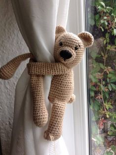 a crocheted teddy bear hanging from the side of a curtain