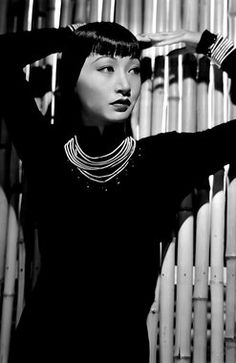 a woman standing in front of a bamboo wall with her hands on her hair and wearing a necklace