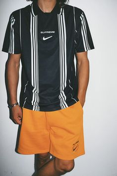 a man in black shirt and yellow shorts standing next to white wall with nike logo on it