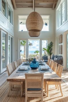 a dining room table with chairs and a blue vase on top of it in front of large windows