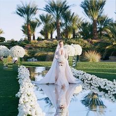 a woman in a wedding dress standing next to white flowers and greenery with palm trees in the background