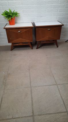 two wooden side tables sitting next to each other on top of a tile floor with a potted plant in the corner