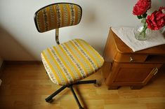 a yellow striped chair sitting next to a wooden dresser with flowers in a vase on top