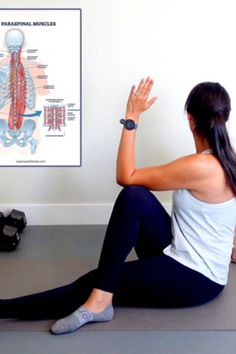 a woman sitting on the floor in front of a wall with her hands up to her chest