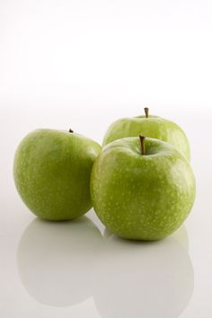 three green apples sitting next to each other on a white surface