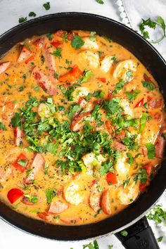 a skillet filled with shrimp and vegetables on top of a white table next to some parsley