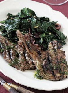 two steaks with spinach on a white plate next to silverware and utensils