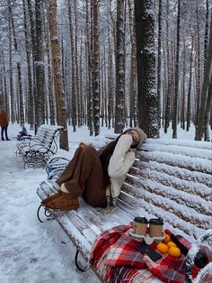 a person is sleeping on a bench in the snow with blankets and oranges next to them