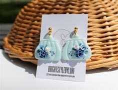 a pair of blue flower earrings sitting on top of a table next to a basket