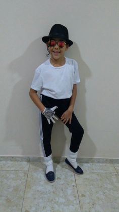 a young boy wearing sunglasses and a hat poses for a photo in front of a wall