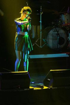 a woman standing on top of a stage next to a drum set in front of her