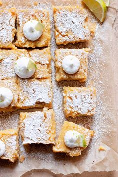 several pieces of dessert on a piece of parchment paper with limes and powdered sugar